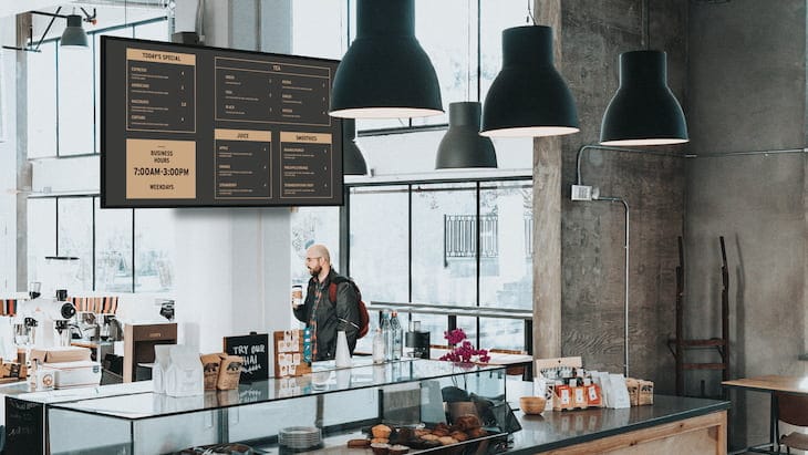 A small, modern cafe with digital menu boards displayed above the counter, showcasing how the Amazon Signage Stick can be used for menu displays in a retail environment