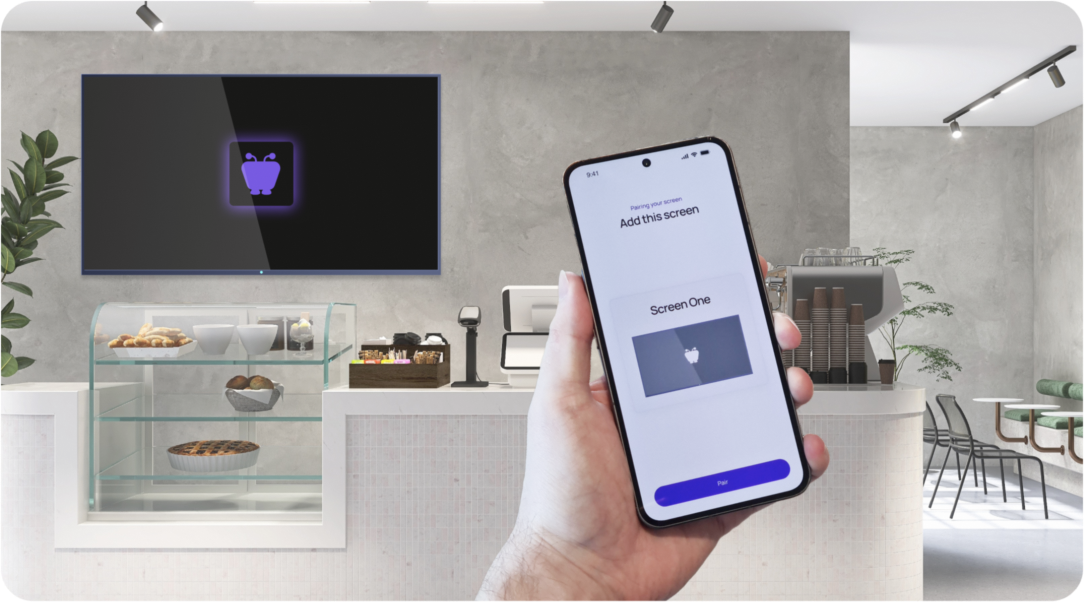 Hand holding a phone with the Fugo app, pairing it to a digital signage screen in a café